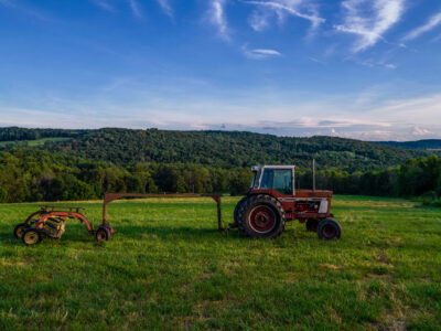 Tractor and hay equipment in a New York farm field surrounded by wooded hills