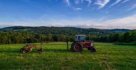 Tractor and hay equipment in a New York farm field surrounded by wooded hills