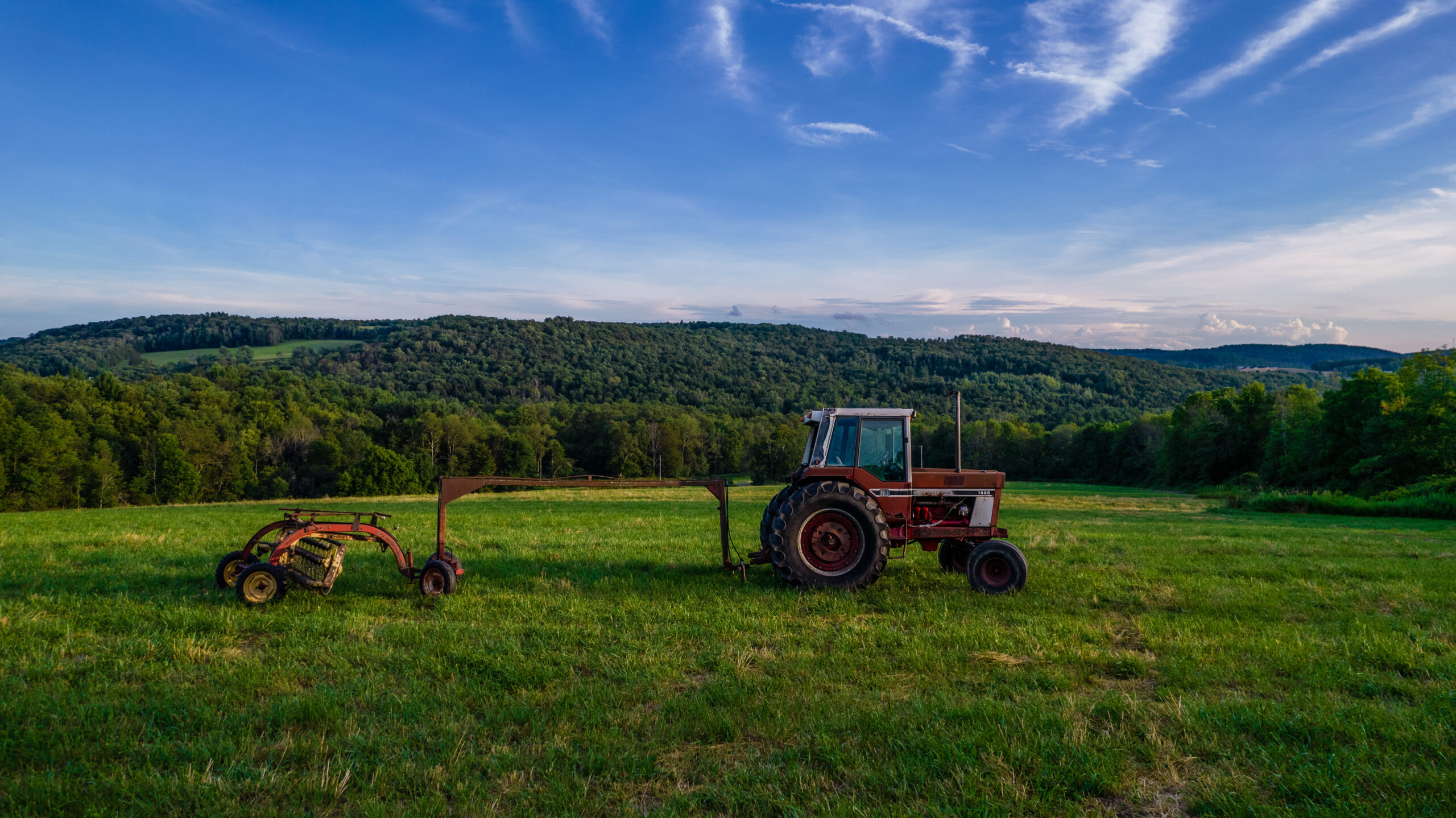 Tractor and hay equipment in a New York farm field surrounded by wooded hills